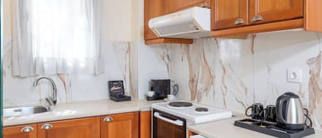 Una cocina compacta con armarios de madera, horno empotrado, cafetera y hervidor sobre la encimera.