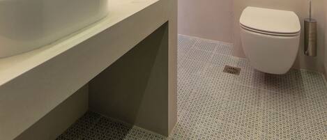 Un baño moderno con un lavamanos grande blanco, un inodoro y una zona de ducha.
