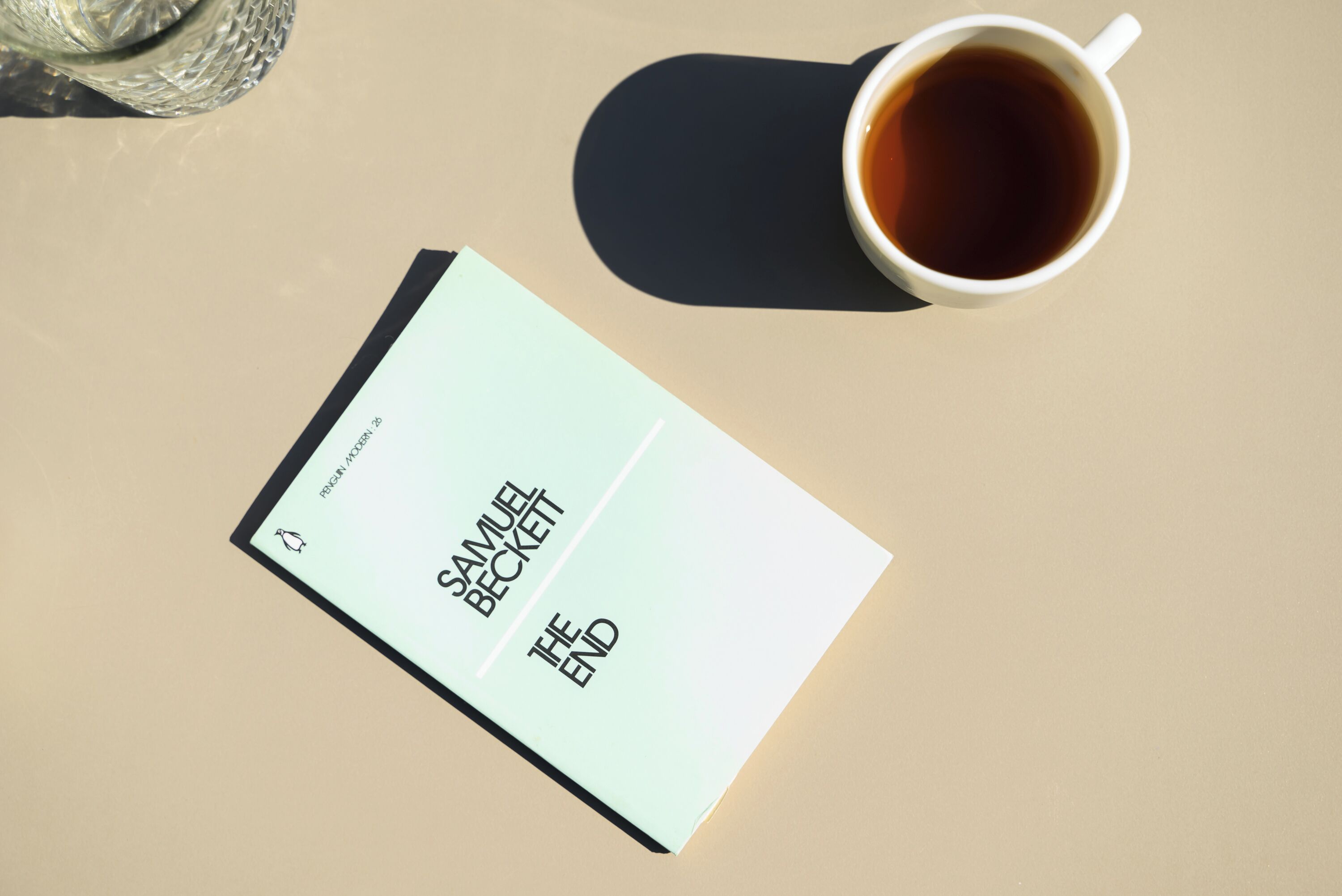 A cup of coffee and a book titled 'The End' by Samuel Beckett on a table.