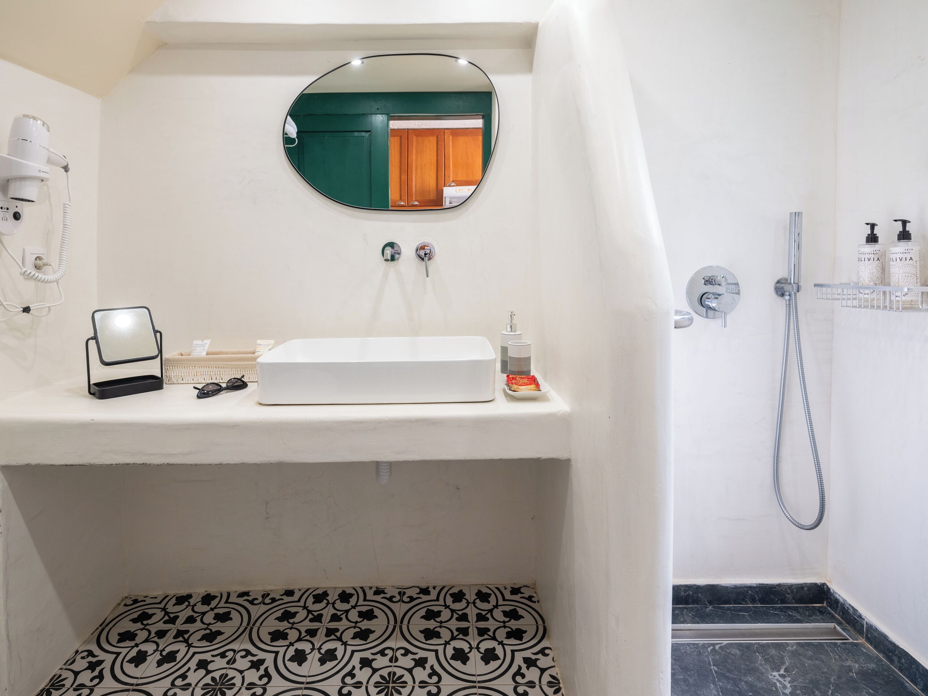 A bathroom with a white sink, a mirror, a handheld showerhead, and a patterned floor.