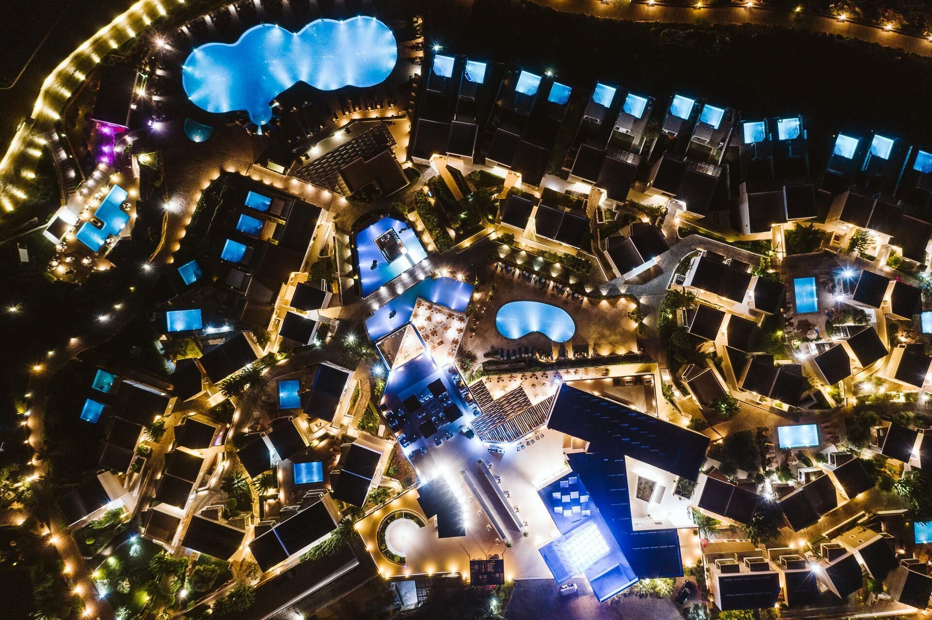 Eine Luftaufnahme eines Resorts mit mehreren Schwimmbecken, darunter ein großes zentrales Becken, sowie verschiedenen Gästeunterkünften.