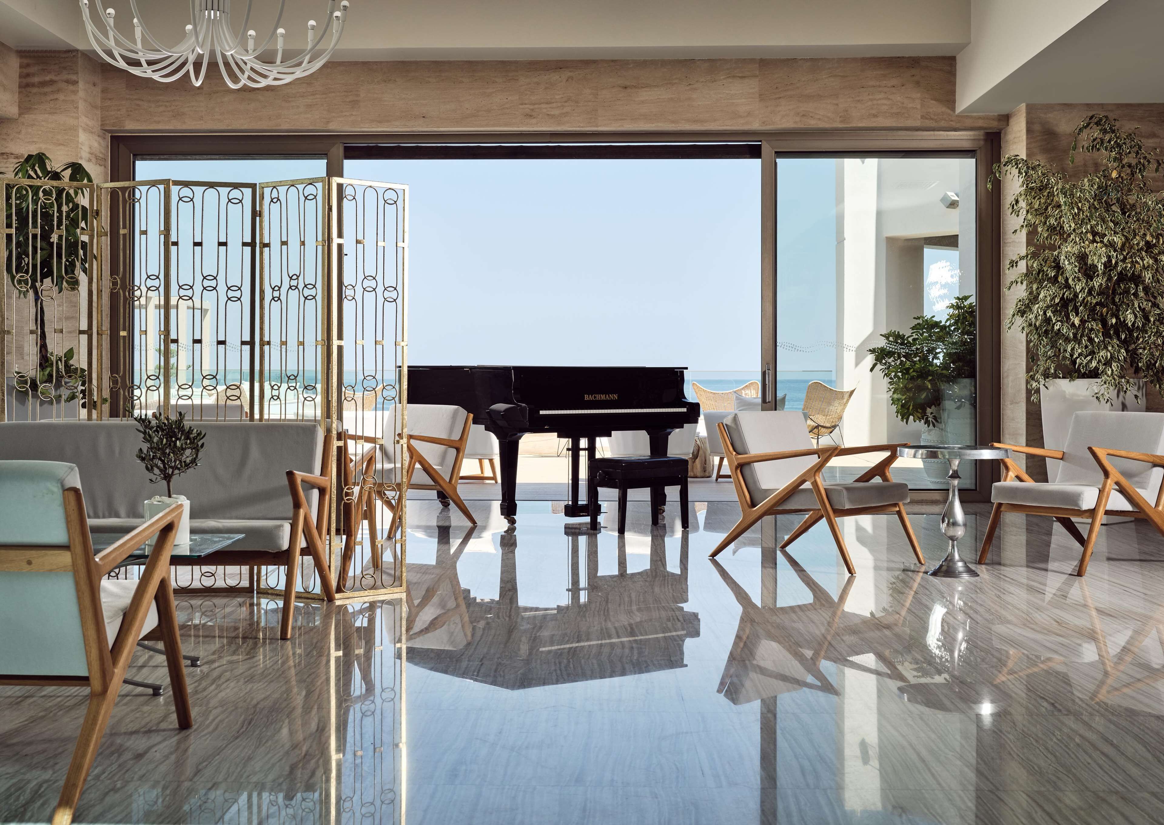 Ein geräumiges Wohnzimmer mit einem Flügel, moderner Möbel und einem großen Glasbalkon mit Blick aufs Meer.