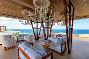 A spacious outdoor seating area with modern furniture and a large chandelier, overlooking the ocean. - The Royal Blue (Mylopotamos)