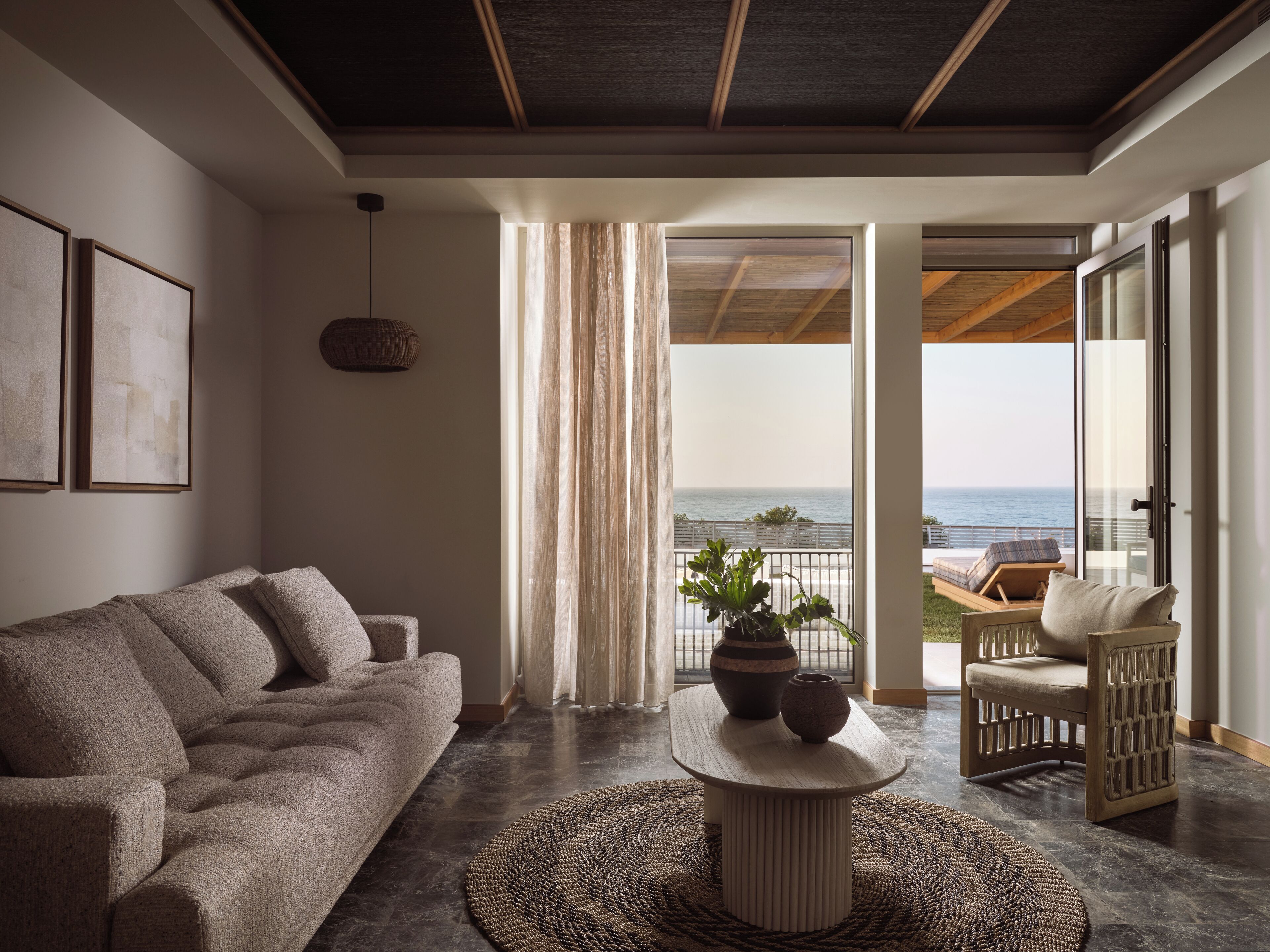 A modern living room with a sofa, a coffee table, and a view of the ocean through large glass doors.