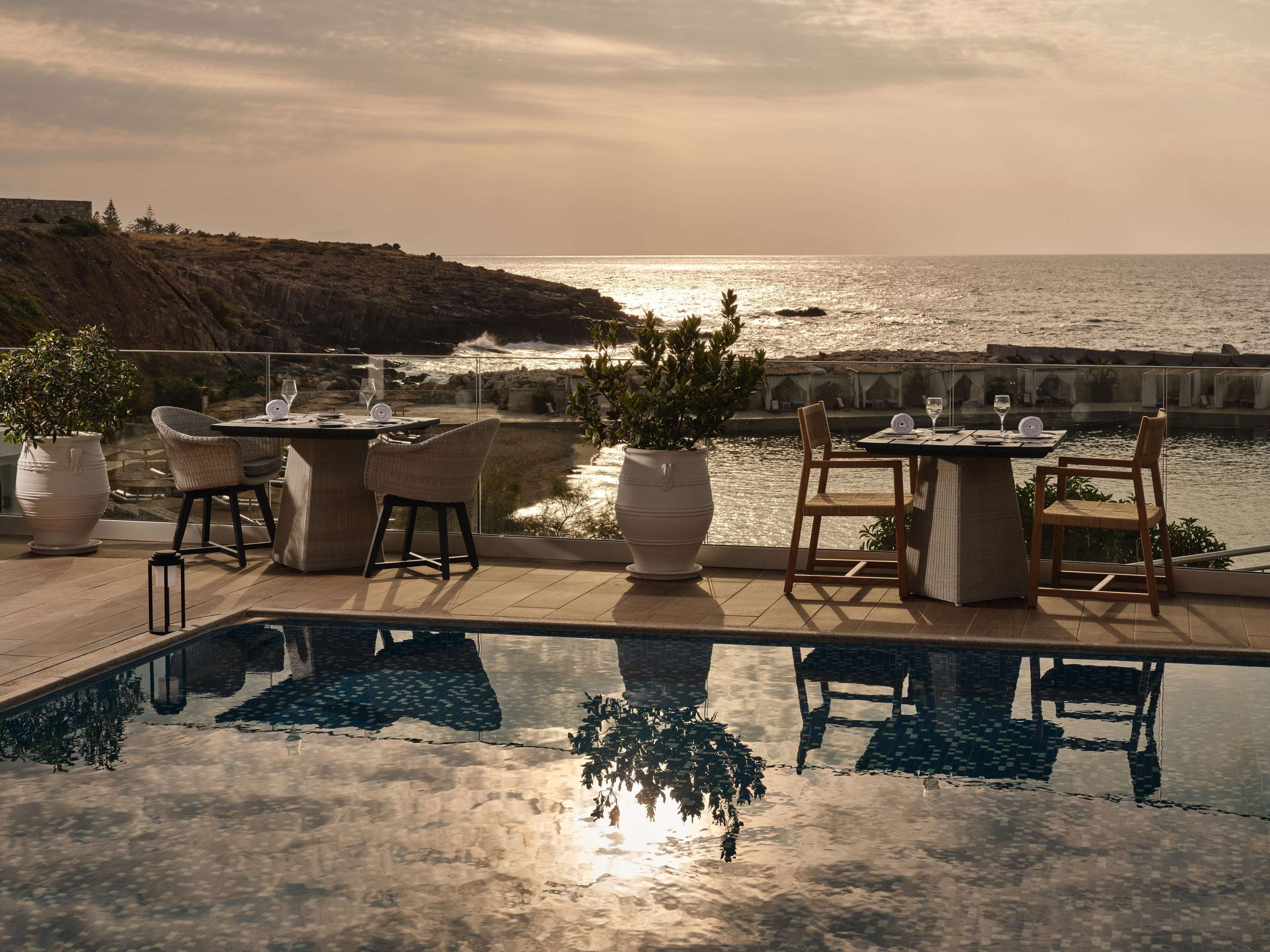 A poolside area with a view of the ocean, outdoor seating, and potted plants.