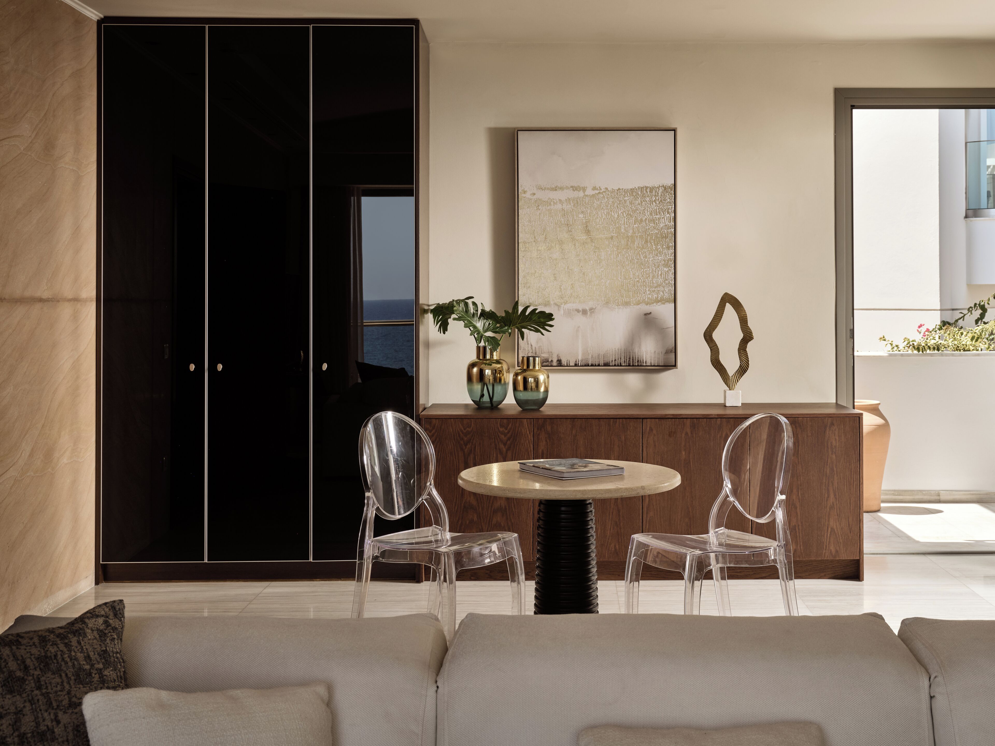 A modern living room with a sofa, two clear chairs, a round table, a wooden cabinet, and a large abstract painting.