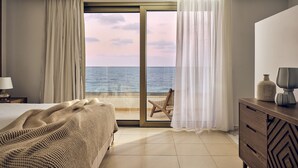 A bedroom with a bed, a chair, a dresser, and a view of the sea through a glass door. - The Royal Blue (Mylopotamos)