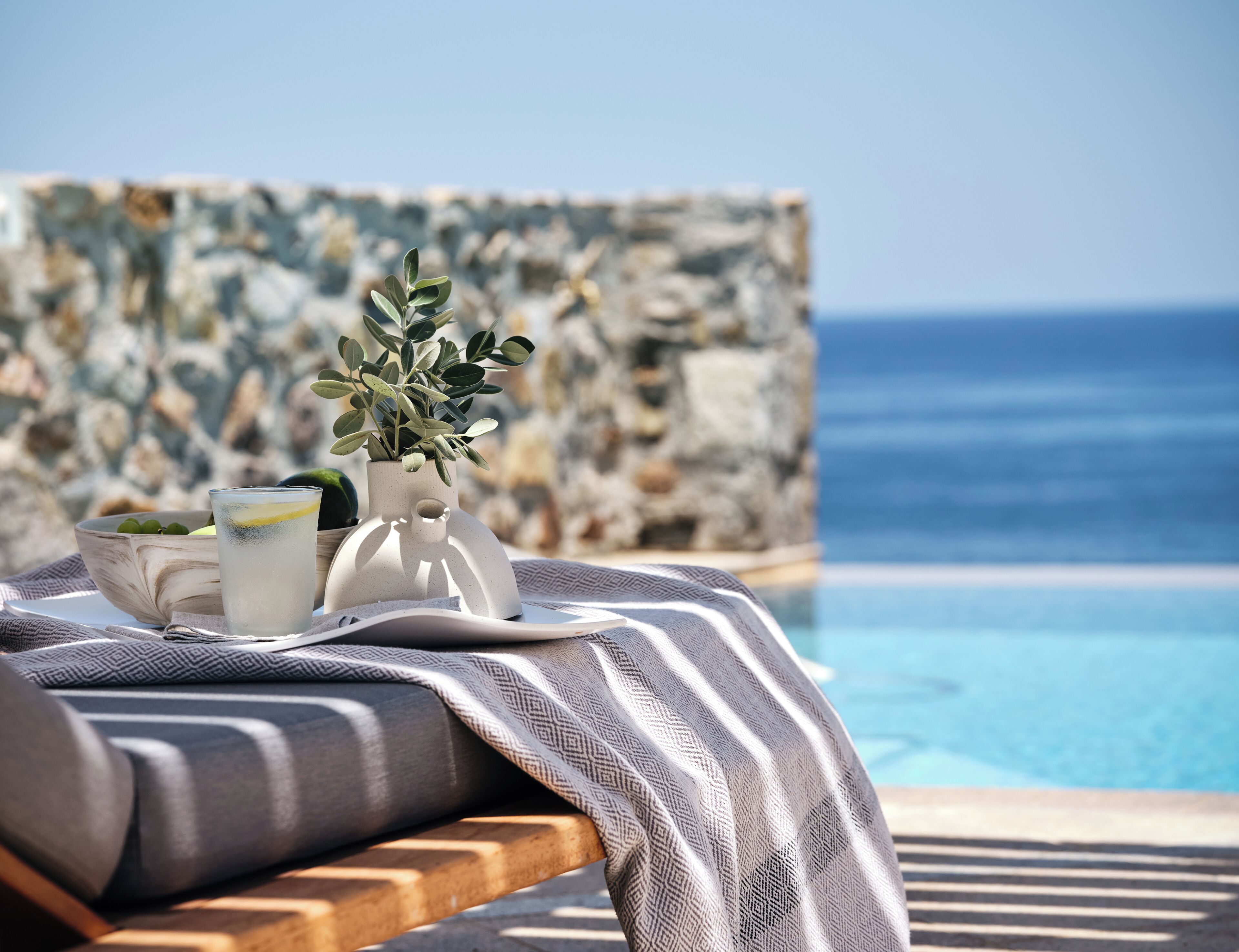 Un salon de bord de piscine avec un mur en pierre, un verre d’eau avec une tranche de citron et une plante en pot.