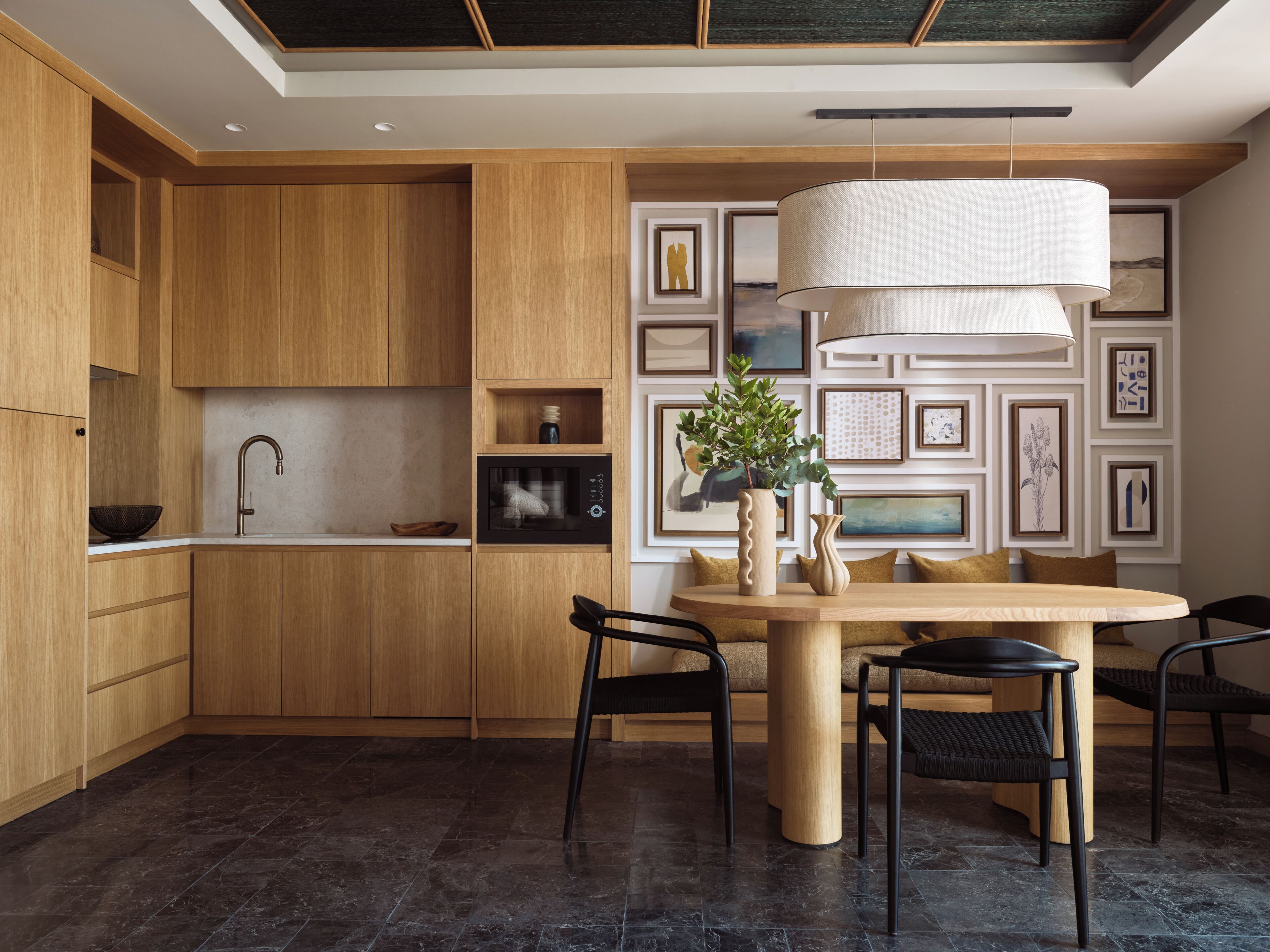 Una cocina moderna con armarios de madera, un lavamanos negro y una mesa de comedor redonda con sillas.