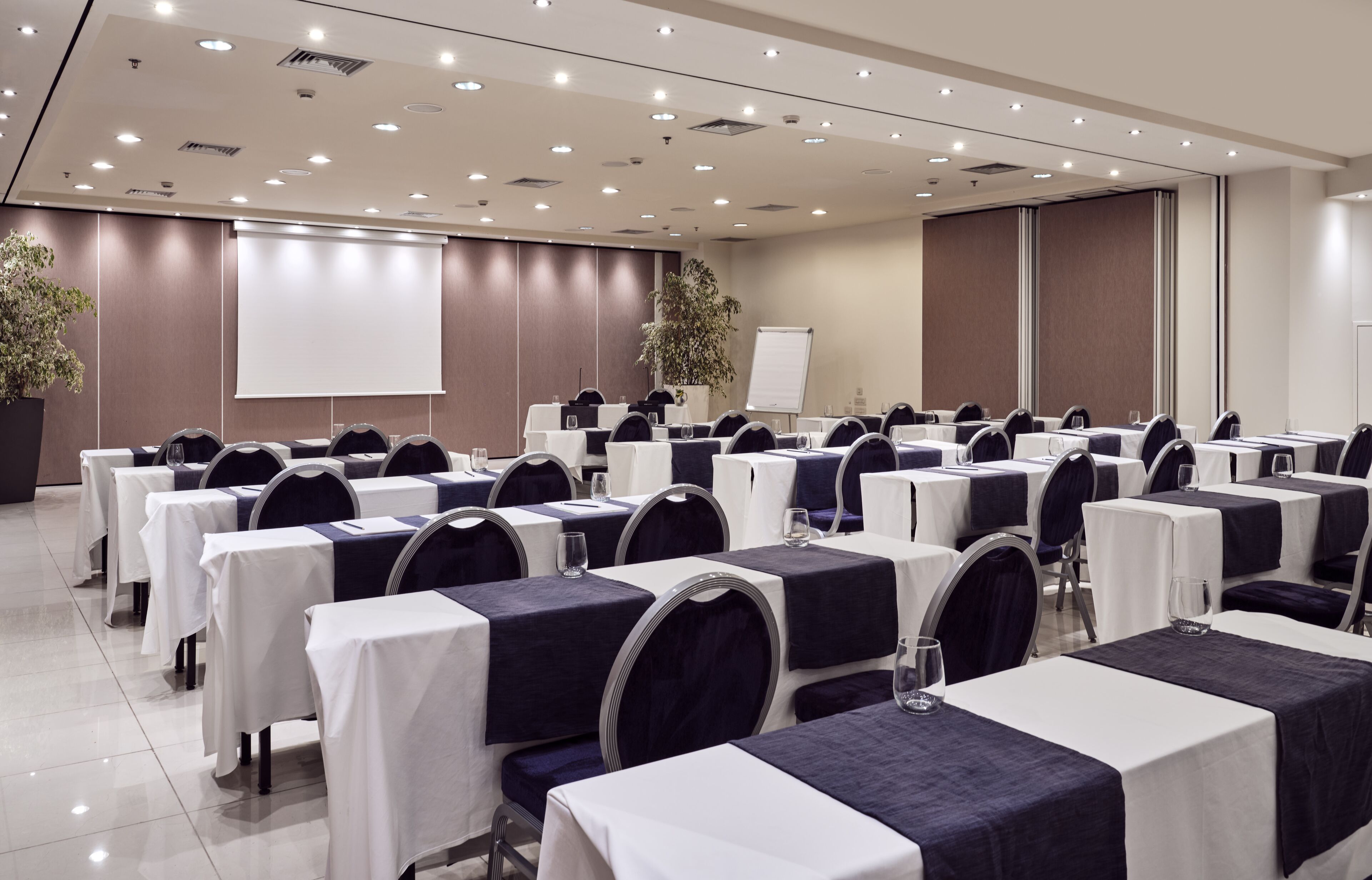 Ein Konferenzraum mit Tischen, Stühlen und einer Projektionsleinwand.