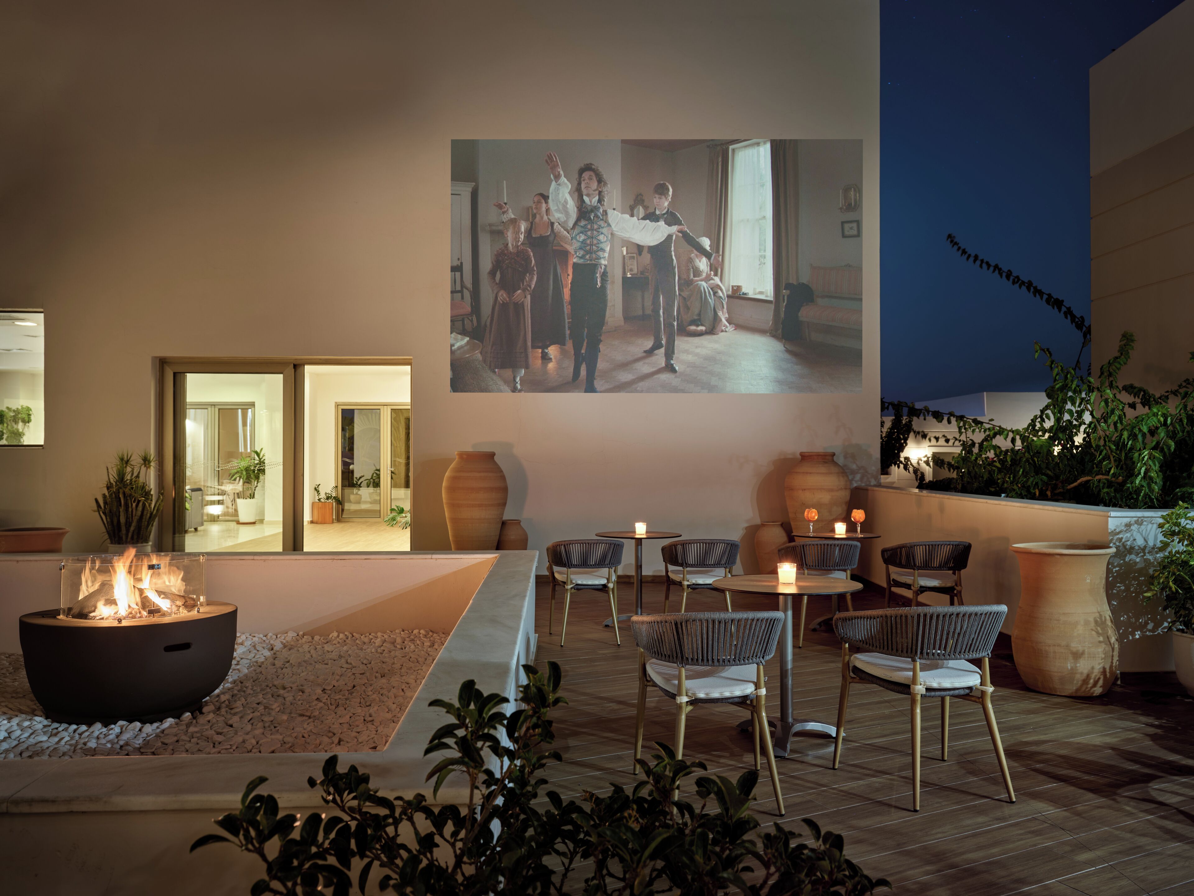 An outdoor seating area with a fire feature, chairs, and a large projection screen.