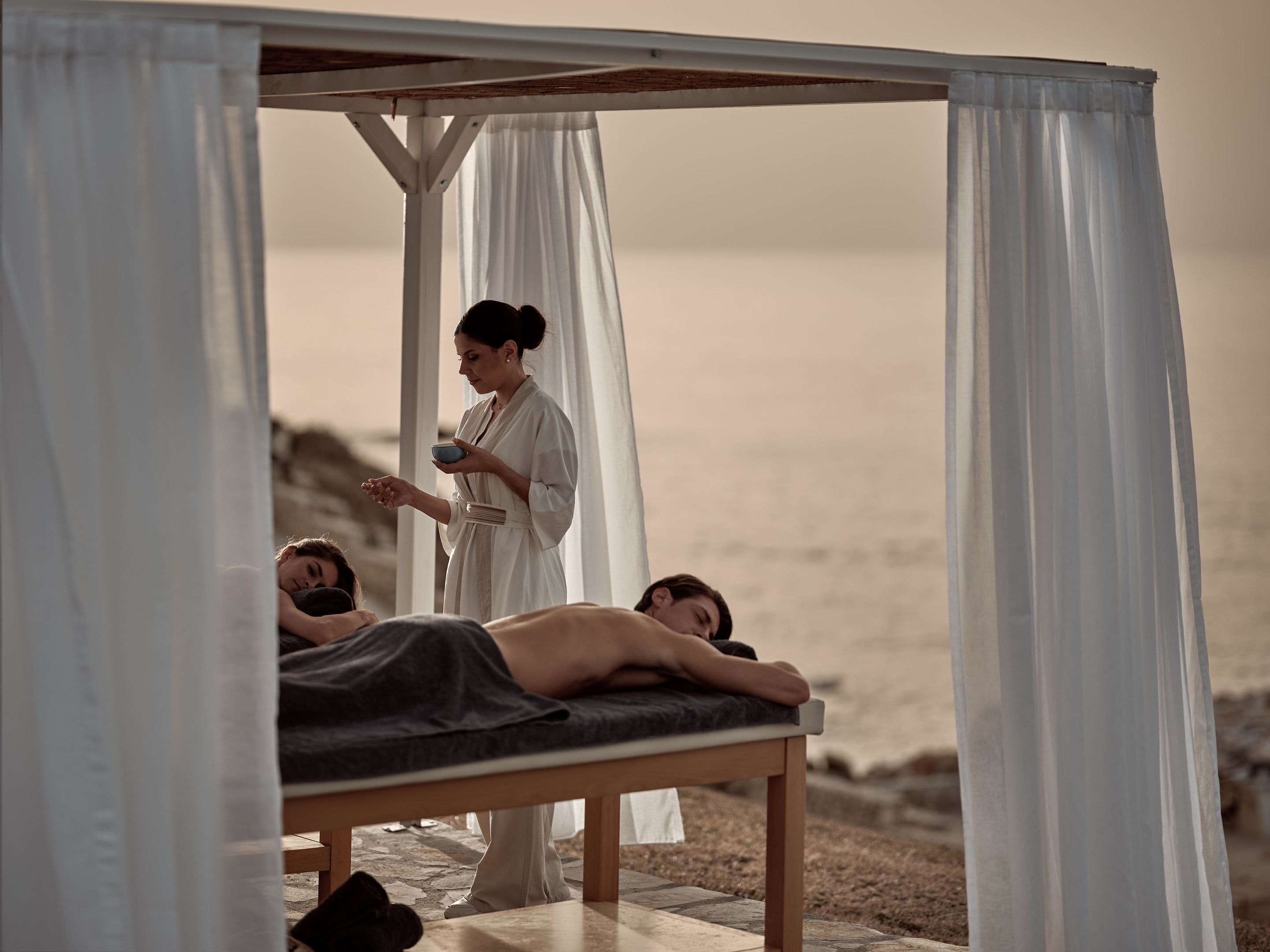 A massage therapy session in a seaside setting with a wooden bench and a canopy.