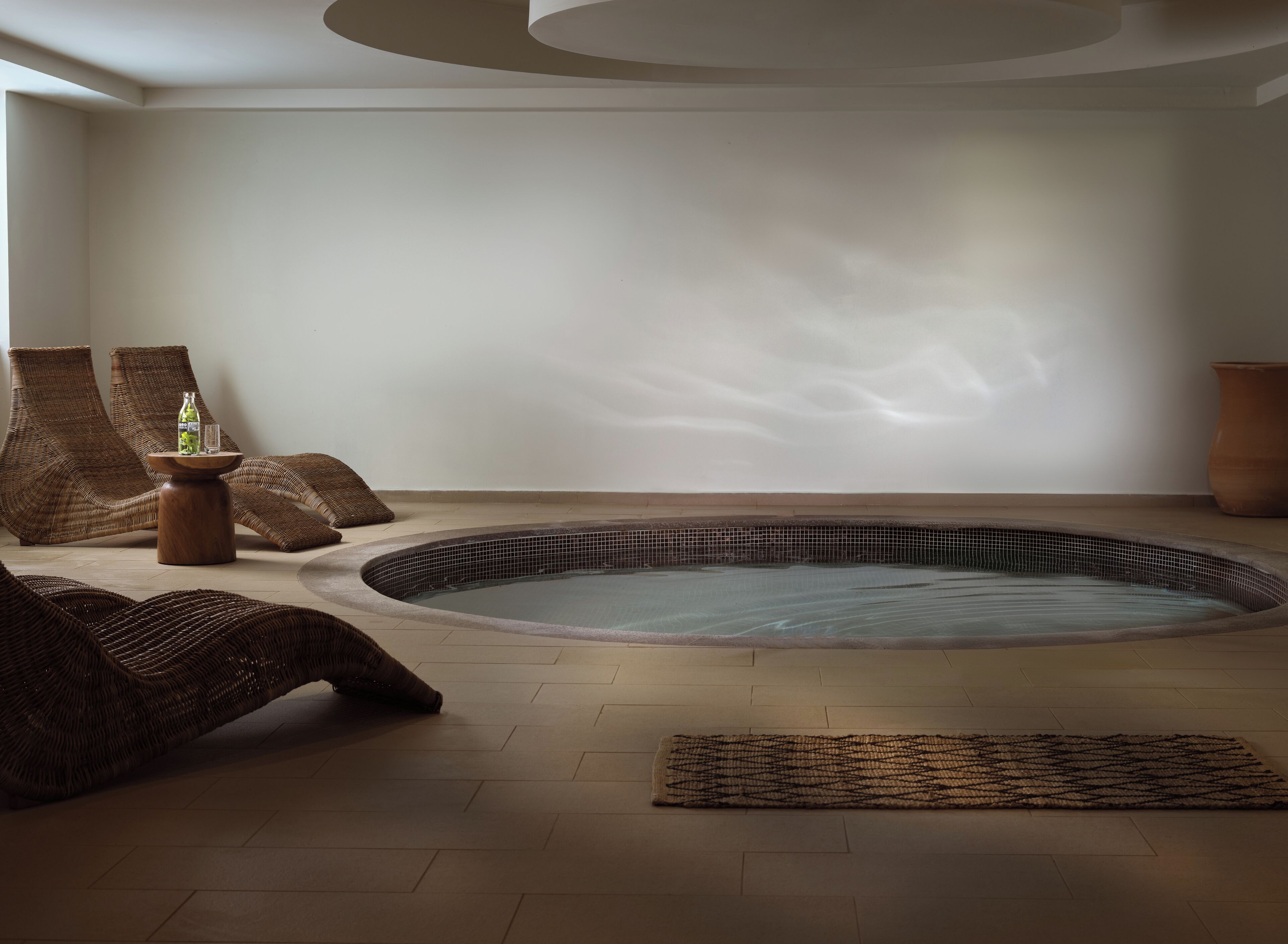 A spa room with a hot tub, wicker chairs, and a small table with a bottle and glass.