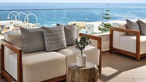 A balcony with a white sofa, patterned cushions, and a wooden stool with a plant. - The Royal Blue (Mylopotamos)