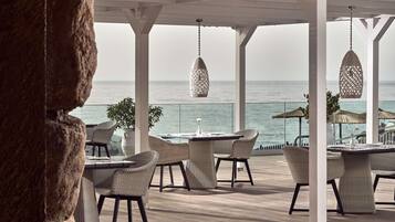 En terrassemiljø ved havet med fletmøbler og hængende lysarmaturer.