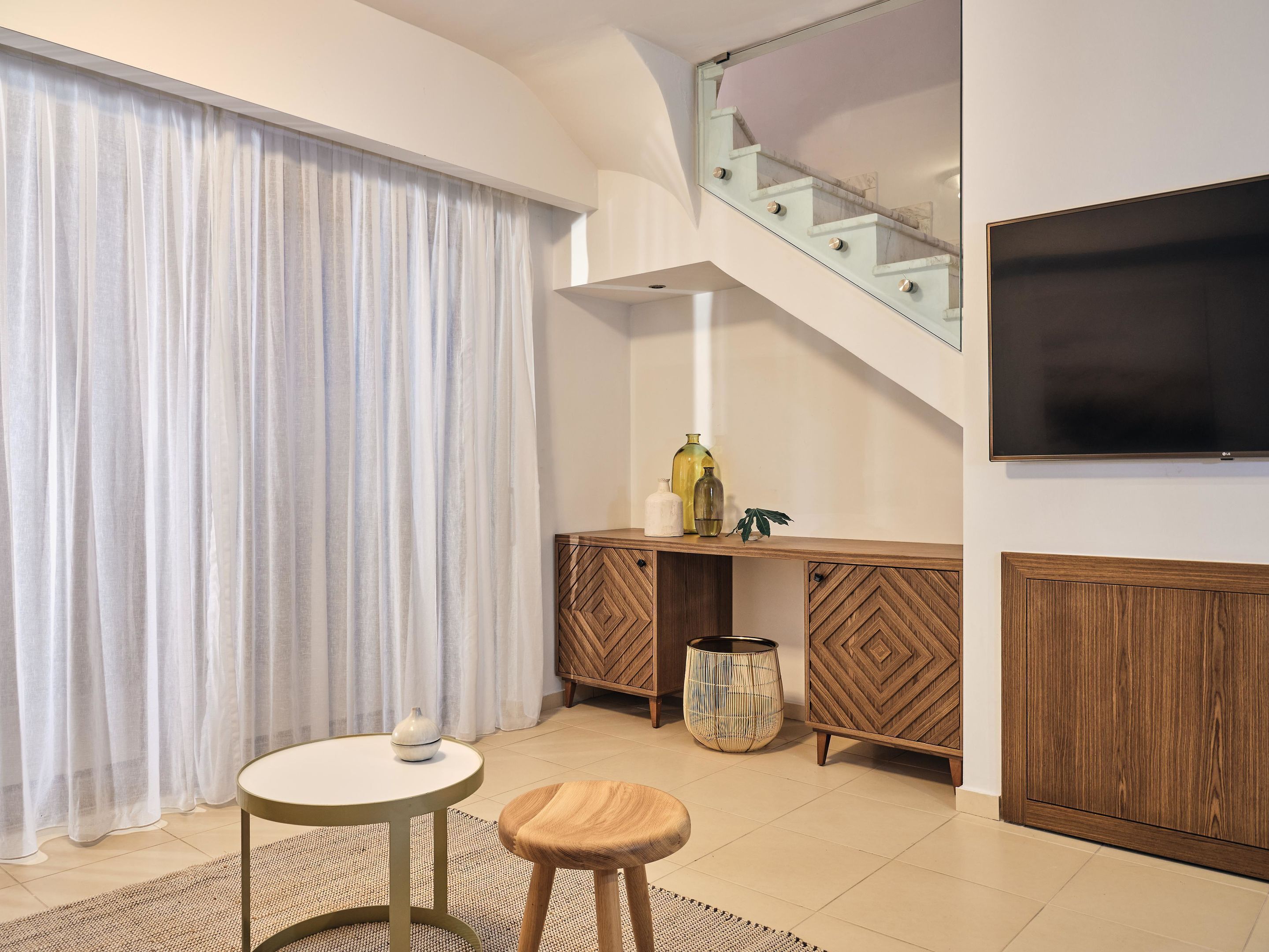 Un salon moderne avec un escalier, un téléviseur, une table ronde, un banc en bois et un meuble.