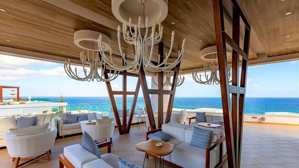 A spacious outdoor seating area with white sofas and tables, overlooking the ocean. - The Royal Blue (Mylopotamos)