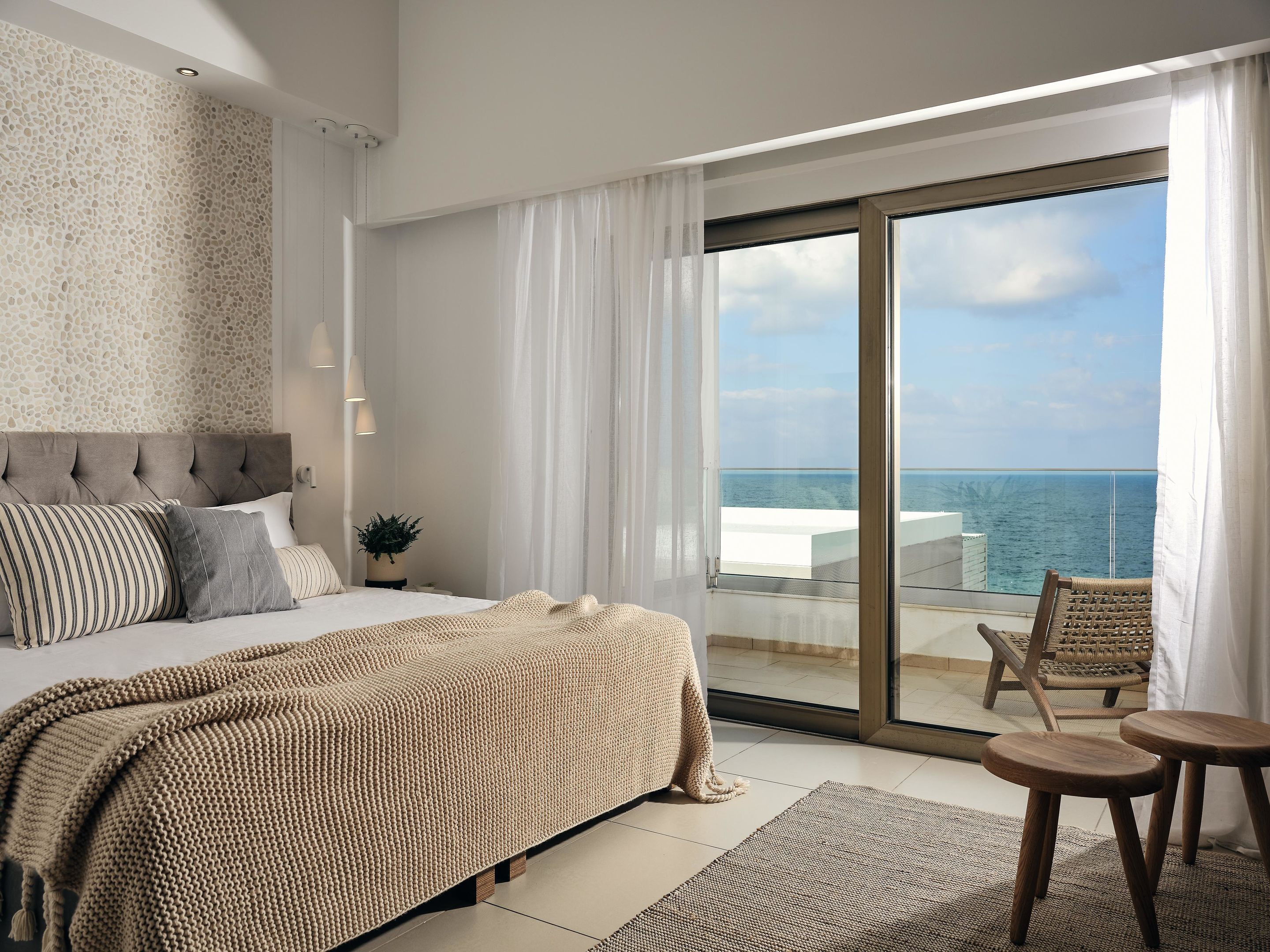 A bedroom with a large bed, a view of the sea, and a balcony with chairs.