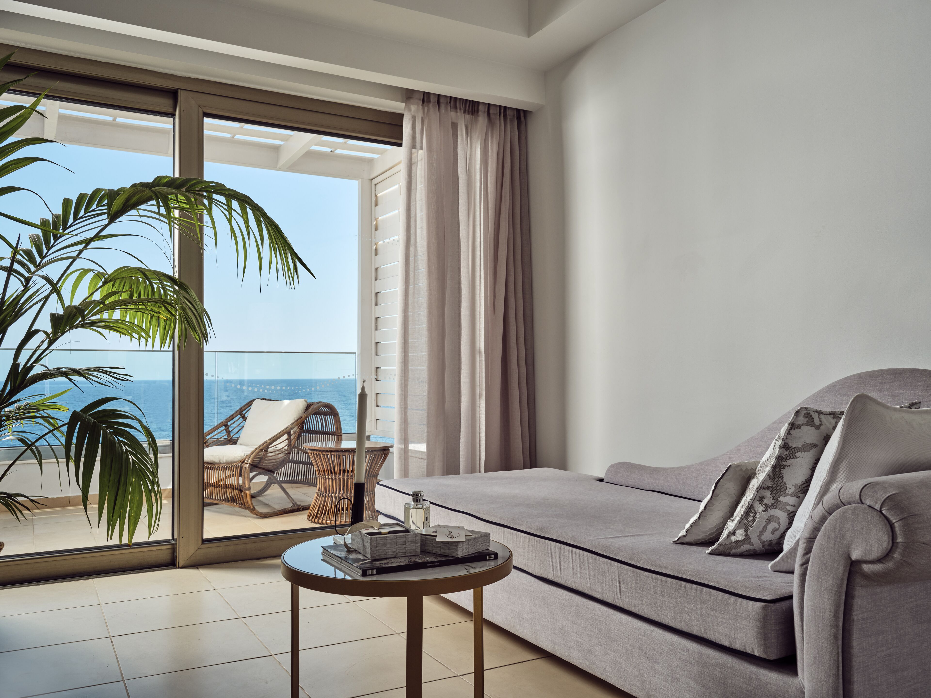 A modern living room with a grey sofa, a small round table, and a view of the ocean through a glass door.