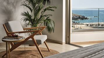 Una habitación moderna con un ventanal grande con vistas al océano, un sillón cómodo con una mesita y una planta grande.