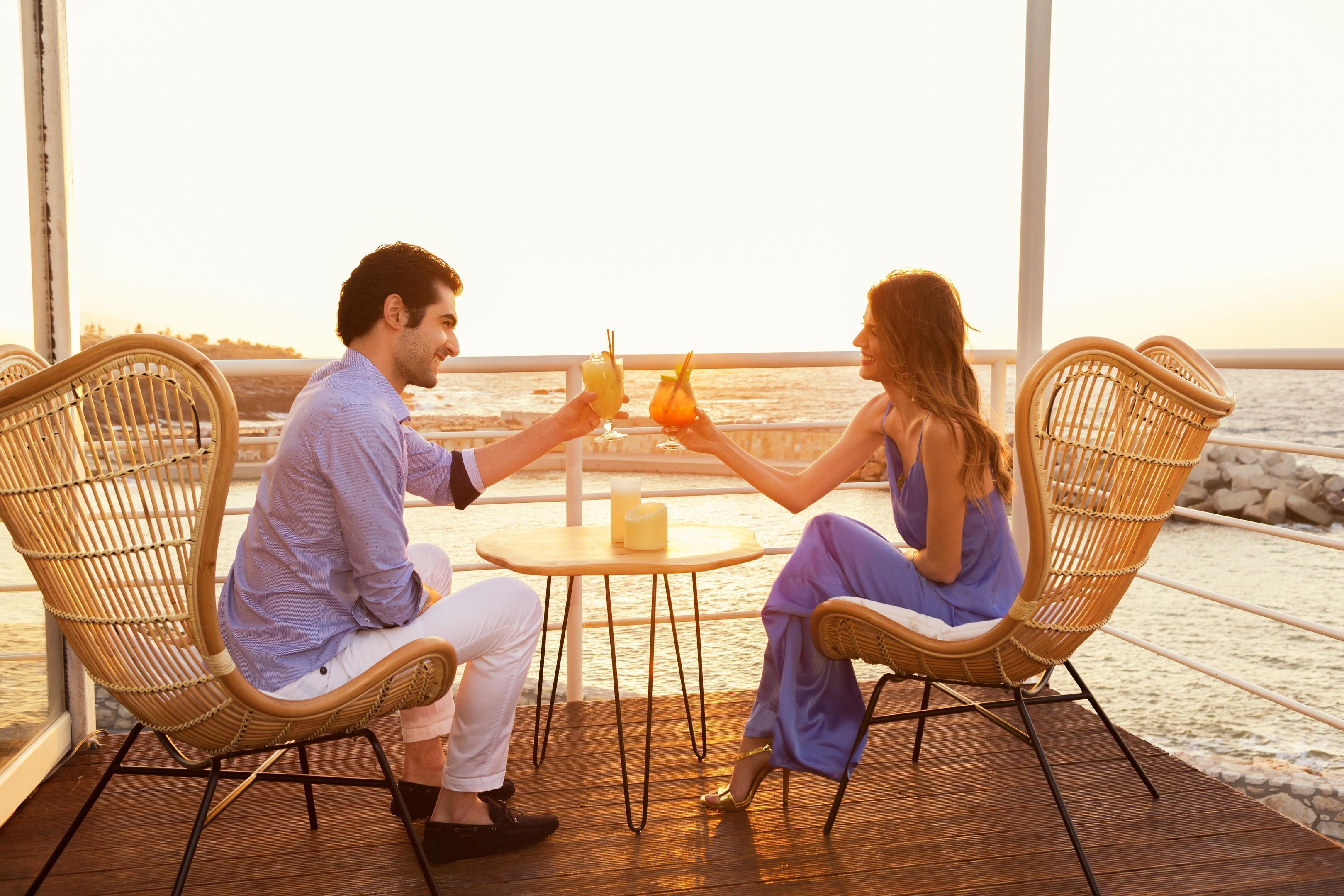 Two people seated at a round table with drinks, overlooking a body of water.