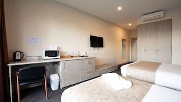 A hotel room with a desk, microwave, TV, and two beds.