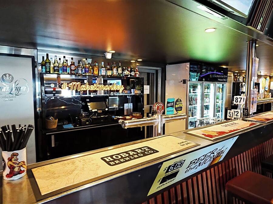 En bardisk med ett stort utbud av spritflaskor, en kaffemaskin och en skylt för Hobart Brewing Co.