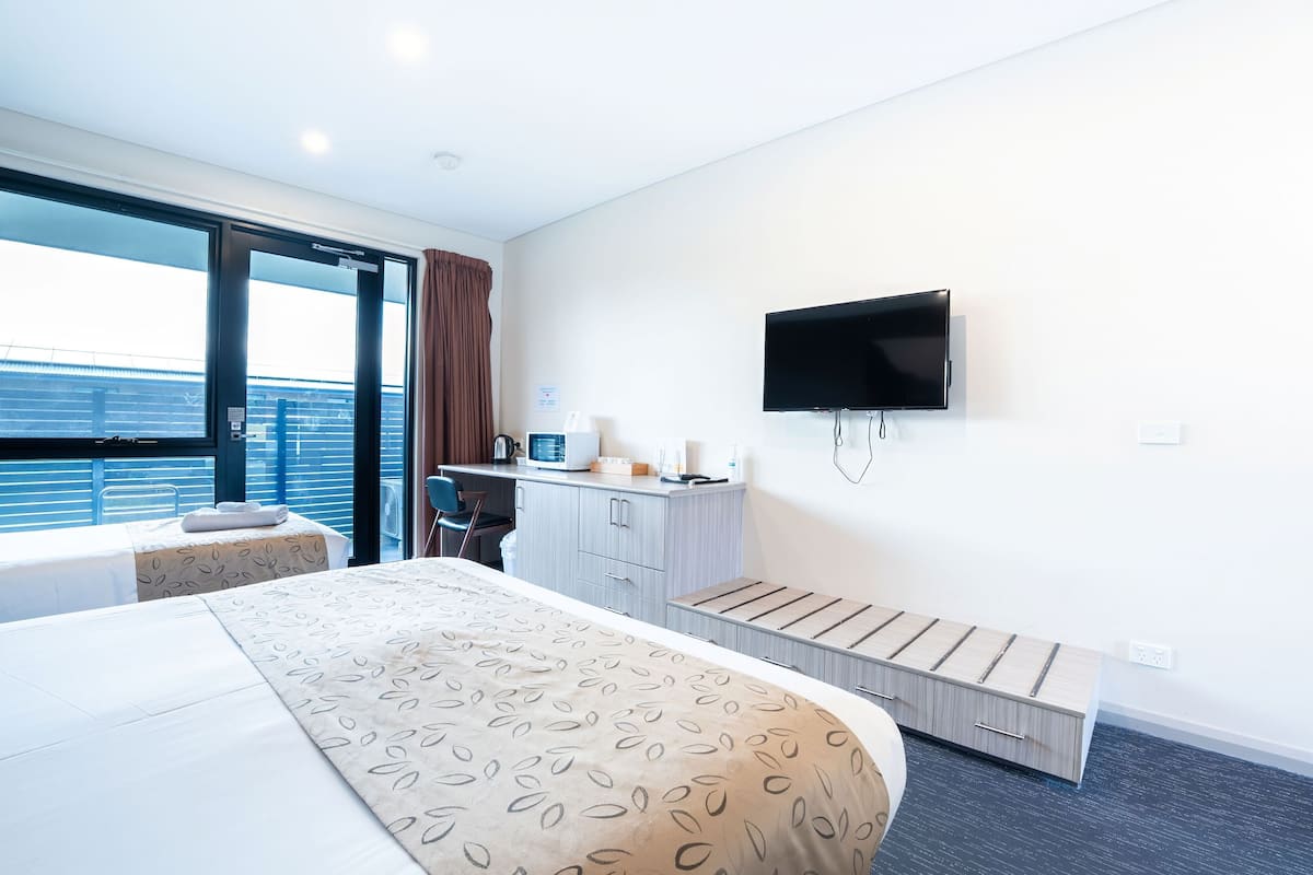 A modern hotel room with a large bed, a desk, a television, and a balcony with a view of the sea.