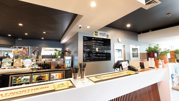 Un comptoir de restaurant avec un tableau affichant le menu, un robinet à bière et un présentoir réfrigéré.