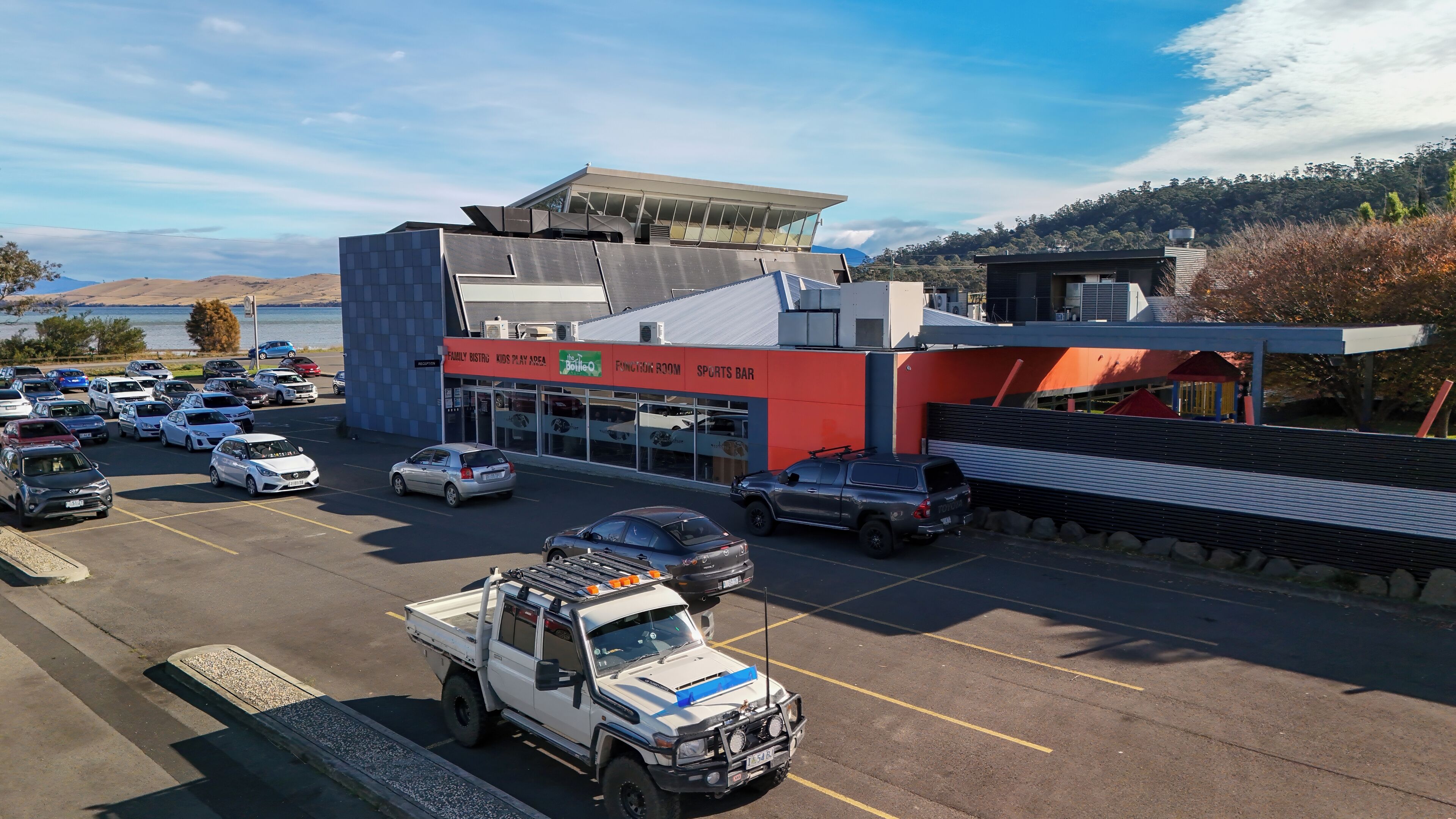 Een parkeerplaats met een gebouw dat een Family Bistrot, kinderspeelplaats, functioneercel en sportbar herbergt.