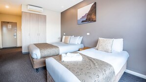 Une chambre d’hôtel avec deux lits, une armoire, un climatiseur et un tableau au mur.