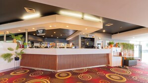 Un hall d’hôtel moderne avec un comptoir d’accueil, un panneau affichant le menu et des plantes en pot.