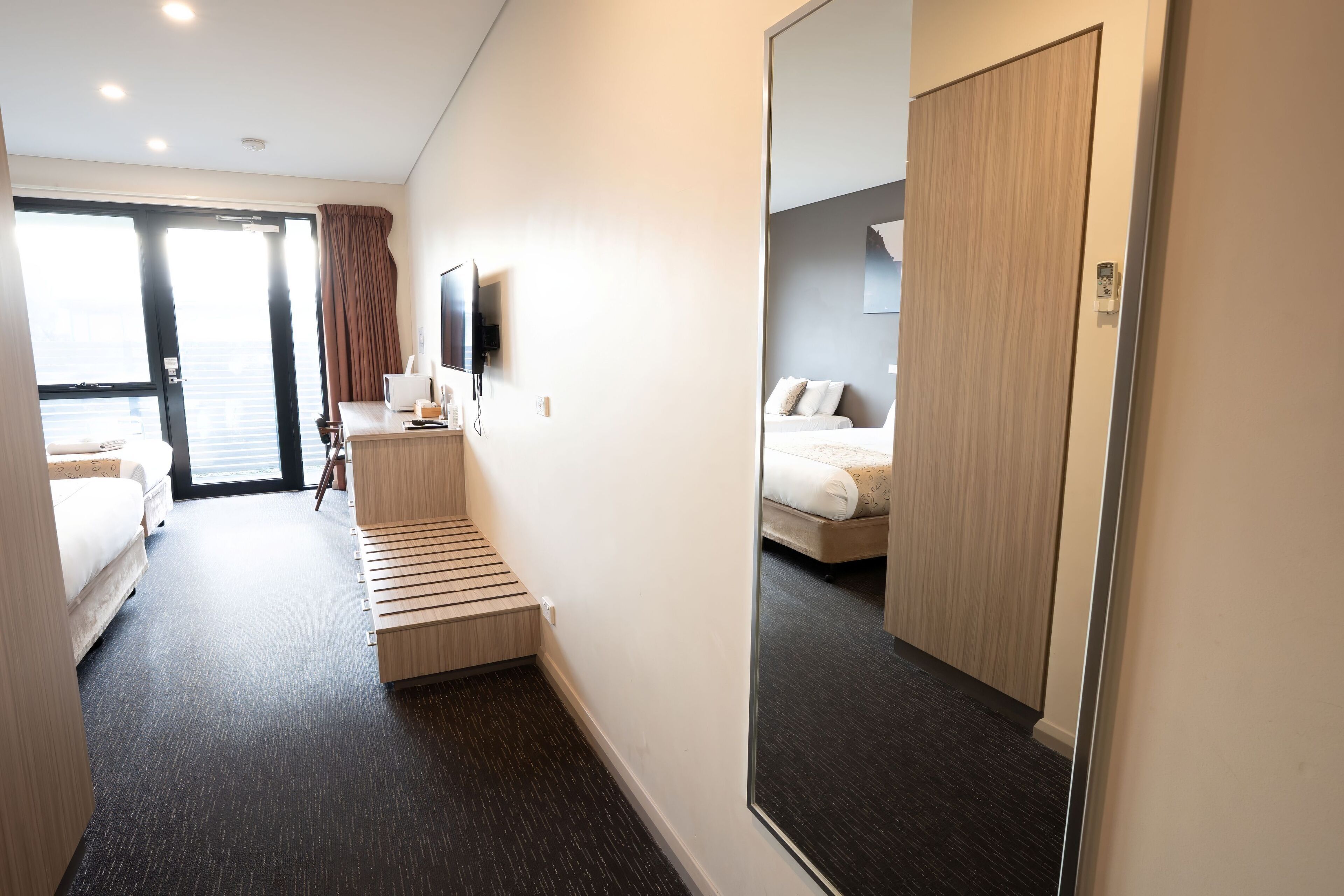 A hotel room with a bed, a desk, a chair, a TV, and a large mirror.