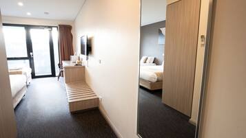 A hotel room with a bed, a desk, a chair, a TV, and a large mirror.