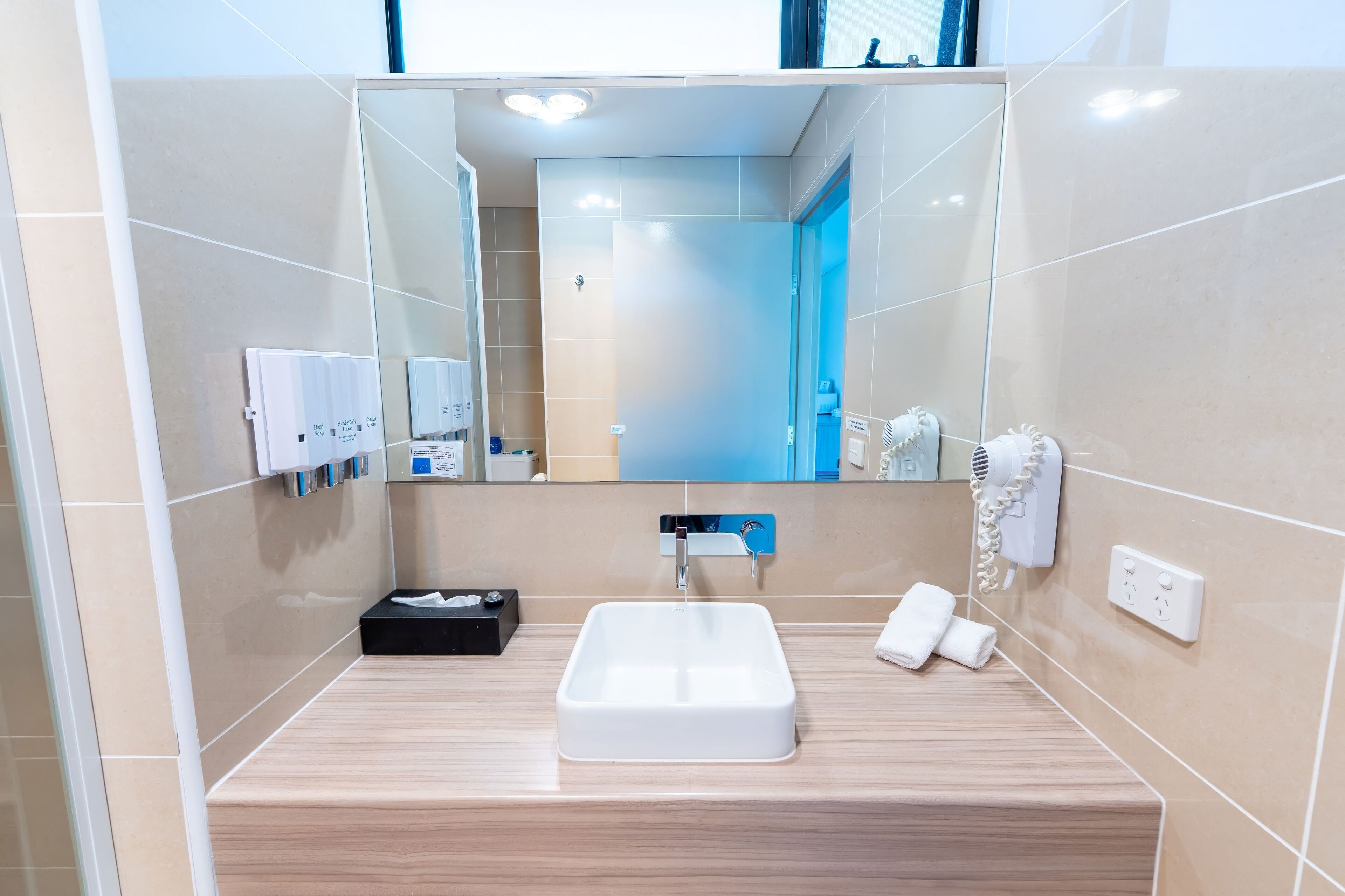 Un baño moderno con un espejo grande, un lavamanos, un perchero para toallas y un secador de pelo.