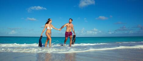 A couple walking on a beach with clear skies and ocean in the background.