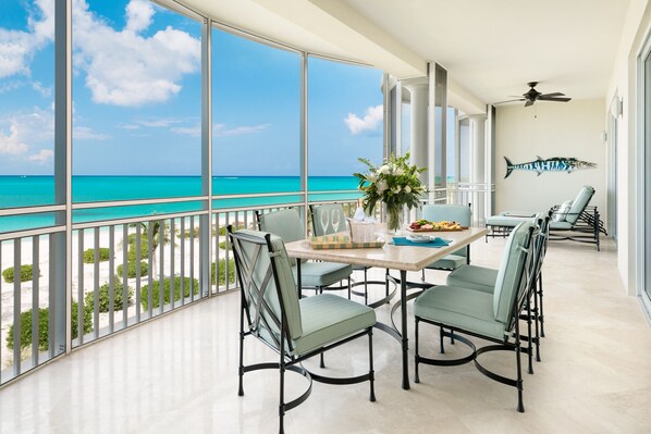 A balcony with a view of the ocean, a table with chairs, and a decorative fish on the wall.