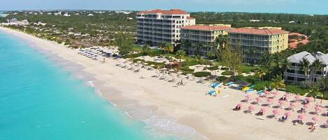 A beachfront hotel with multiple buildings, a sandy beach, and clear turquoise waters.