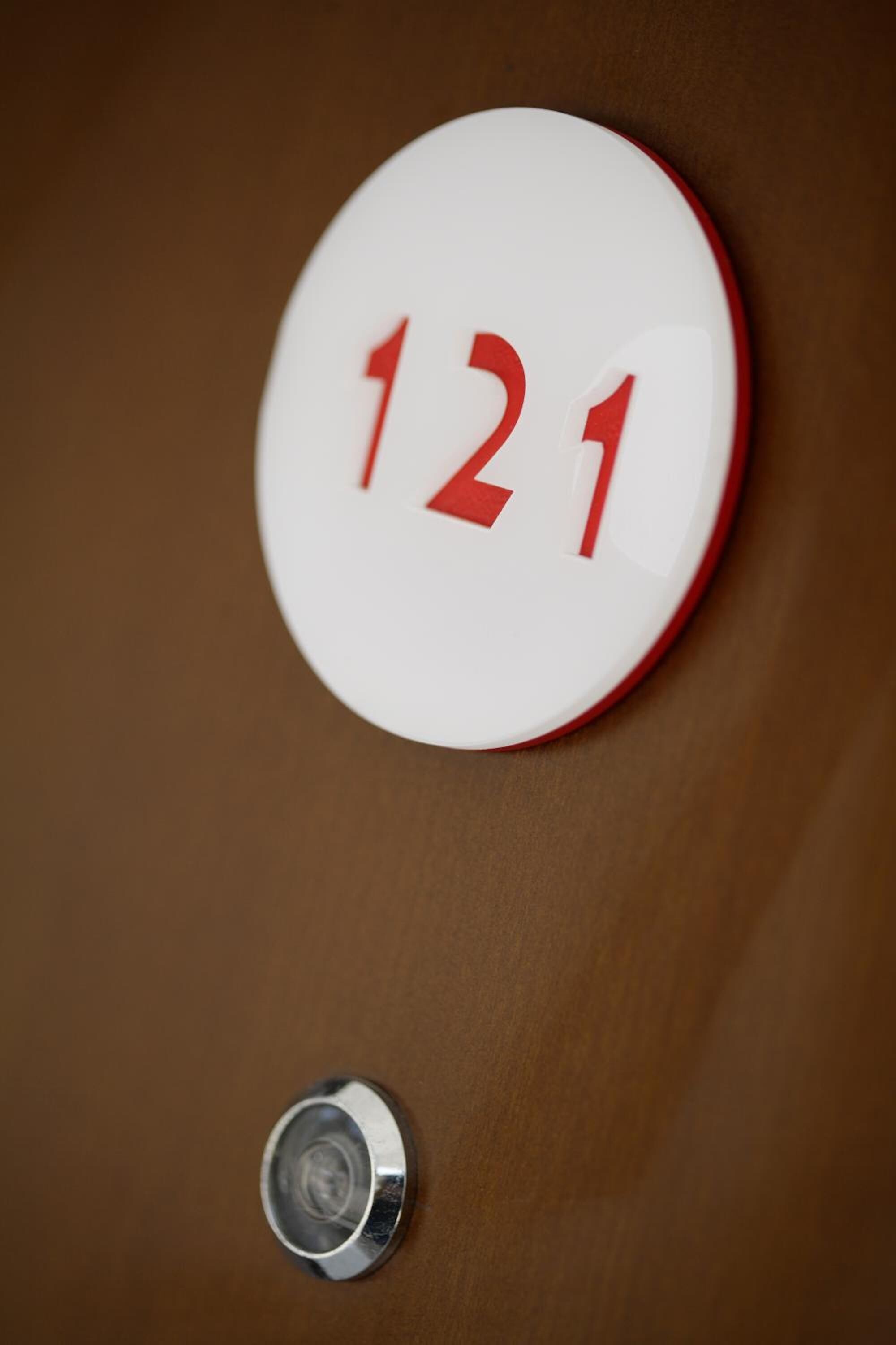 Ein rundes, weißes Schild mit roten Zahlen "121" auf einer braunen Fläche.