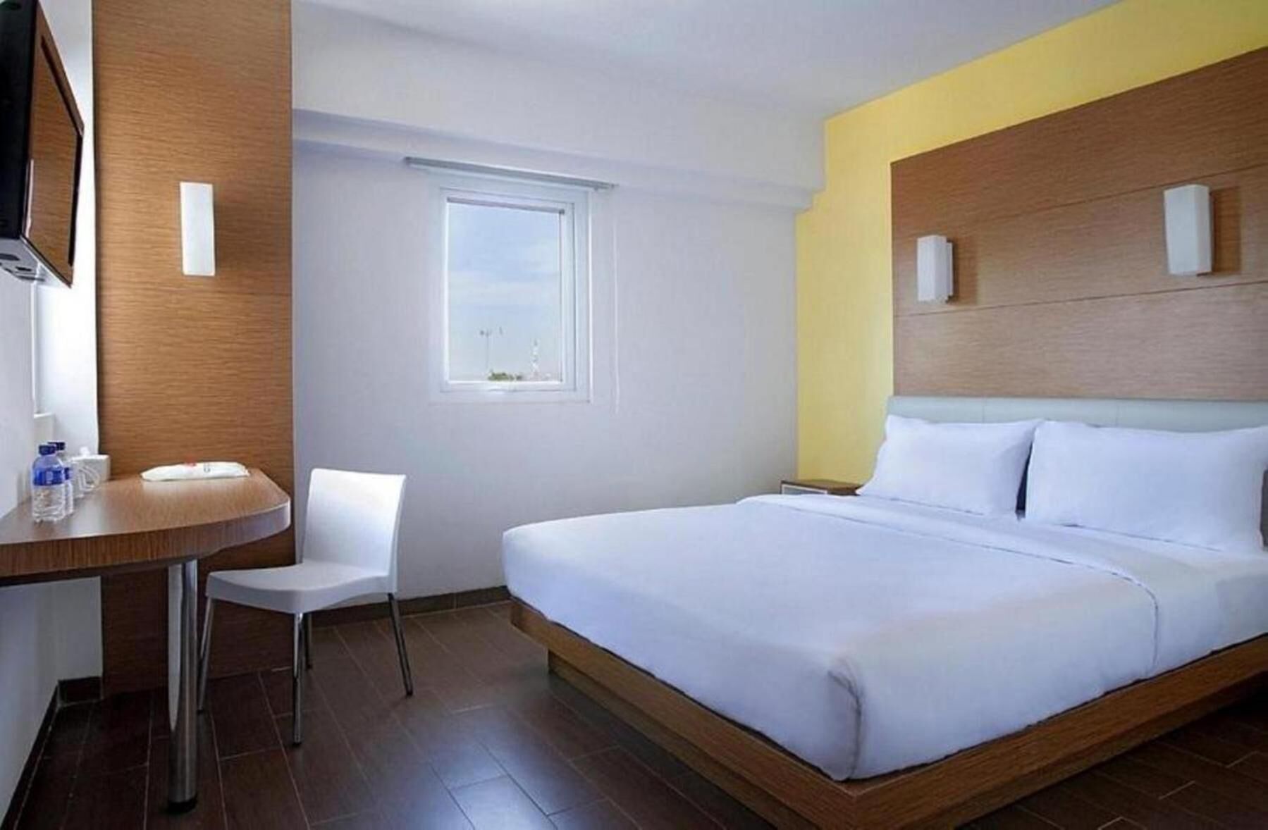 Une chambre d’hôtel avec un lit, un bureau, une chaise, une fenêtre et une vue sur le ciel.