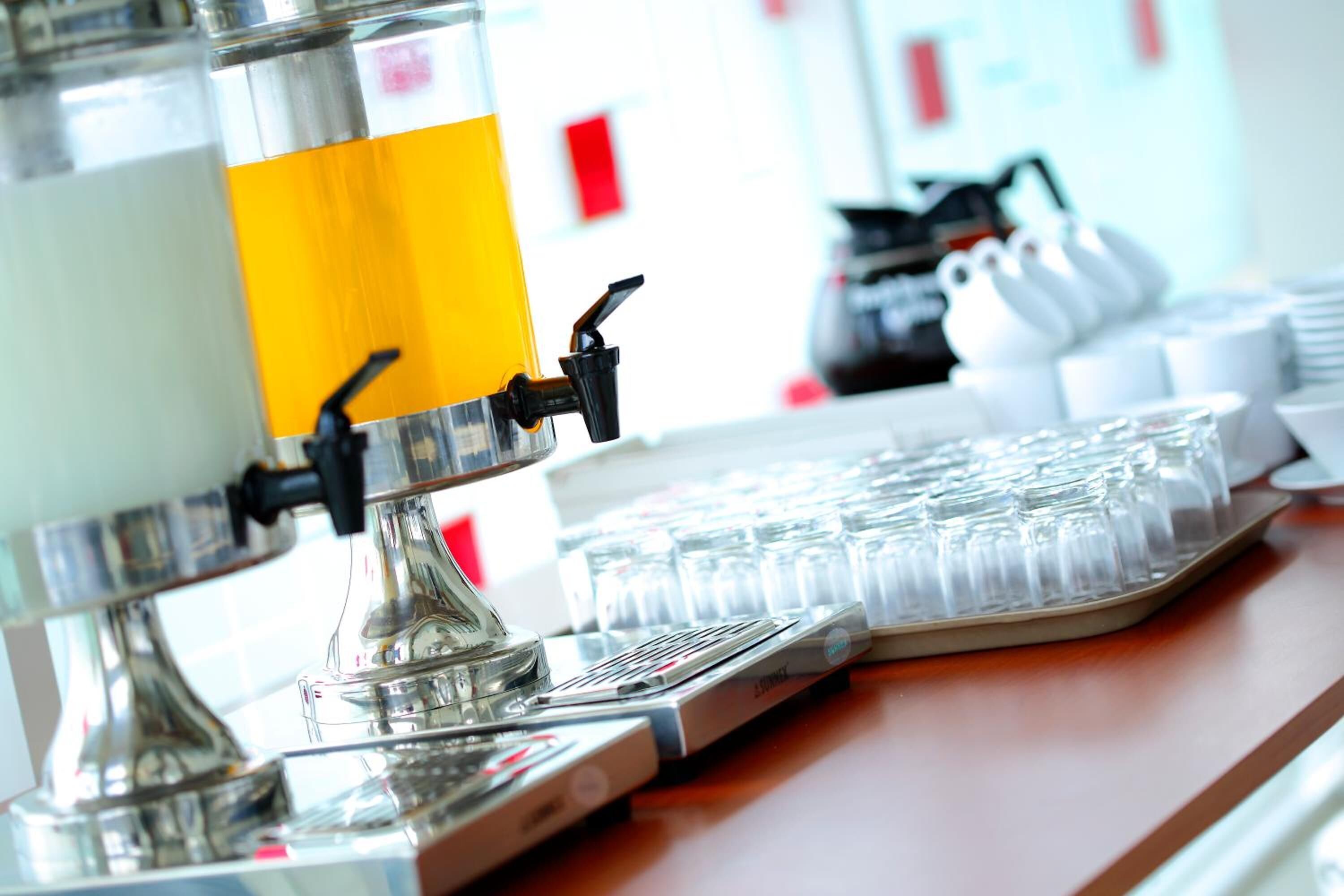 A coffee machine with a yellow panel, a tray of clear glasses, and a coffee grinder in the background.