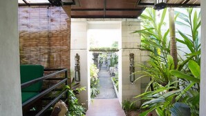 A narrow pathway leading to a covered area with a green sofa and decorative statues.