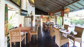 A spacious dining area with wooden tables and chairs, a ceiling fan, and a view of the garden outside.