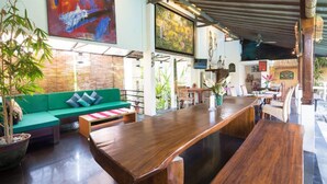 A spacious indoor area with a long wooden table, a green sofa with cushions, and various plants.