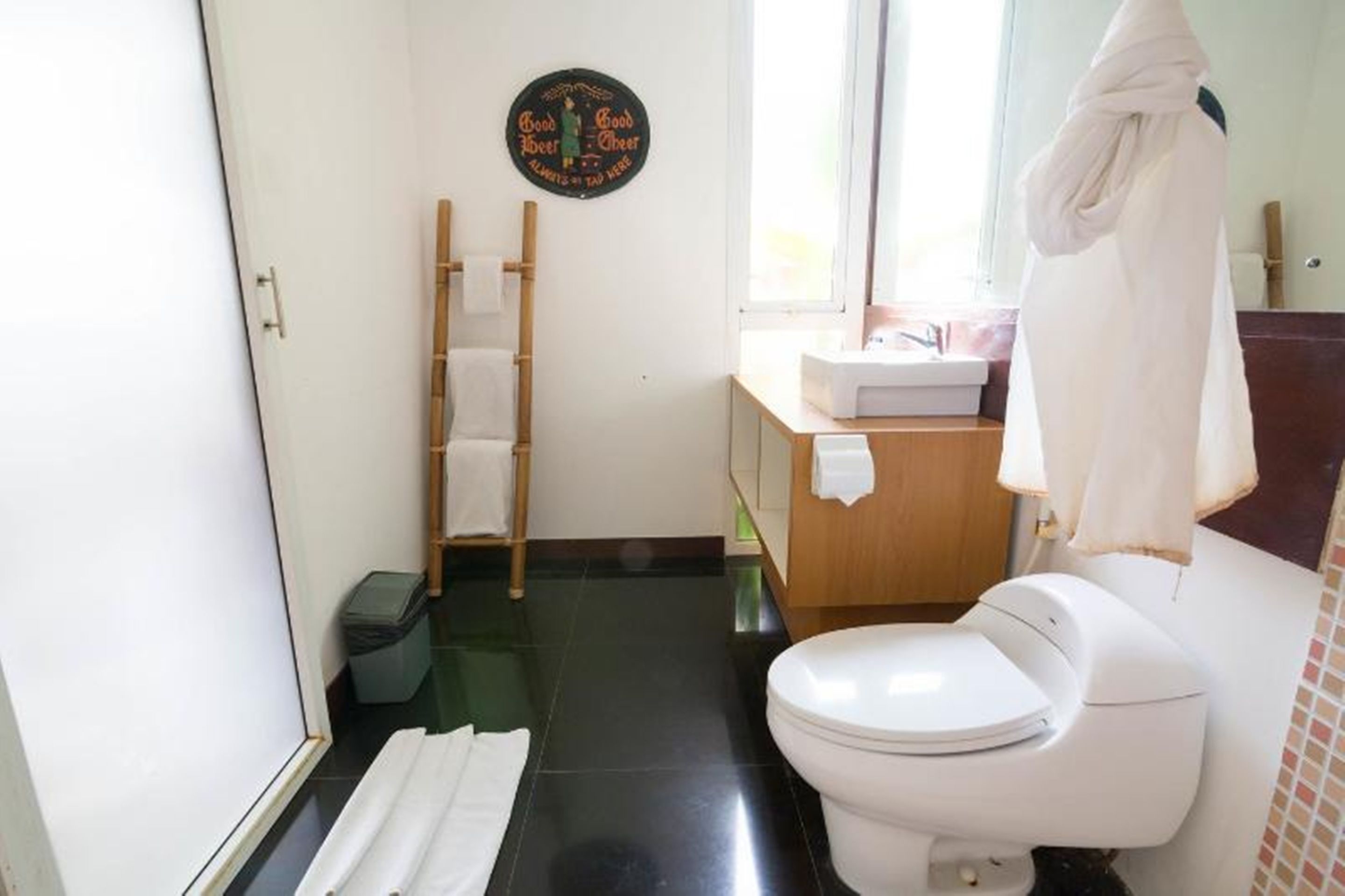 A bathroom with a toilet, a towel rack, a wooden ladder, and a sign on the wall.