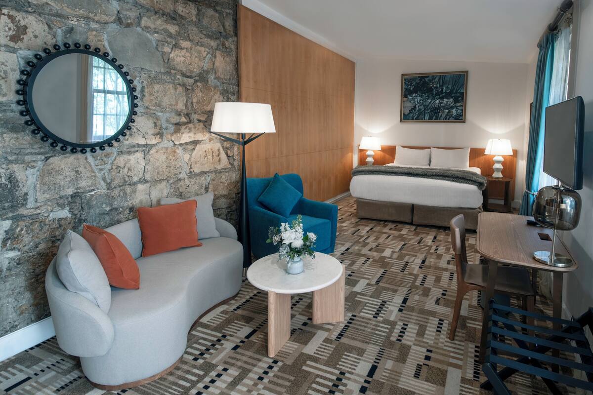 A hotel room with a stone wall, a bed, a sofa, a coffee table, and a TV.