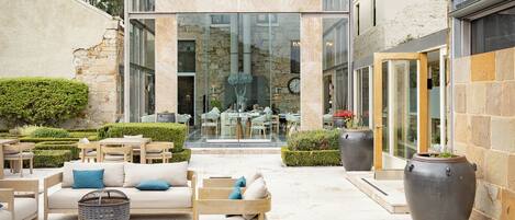 A modern outdoor seating area with a glass-enclosed dining space, stone walls, and a reflective water feature.