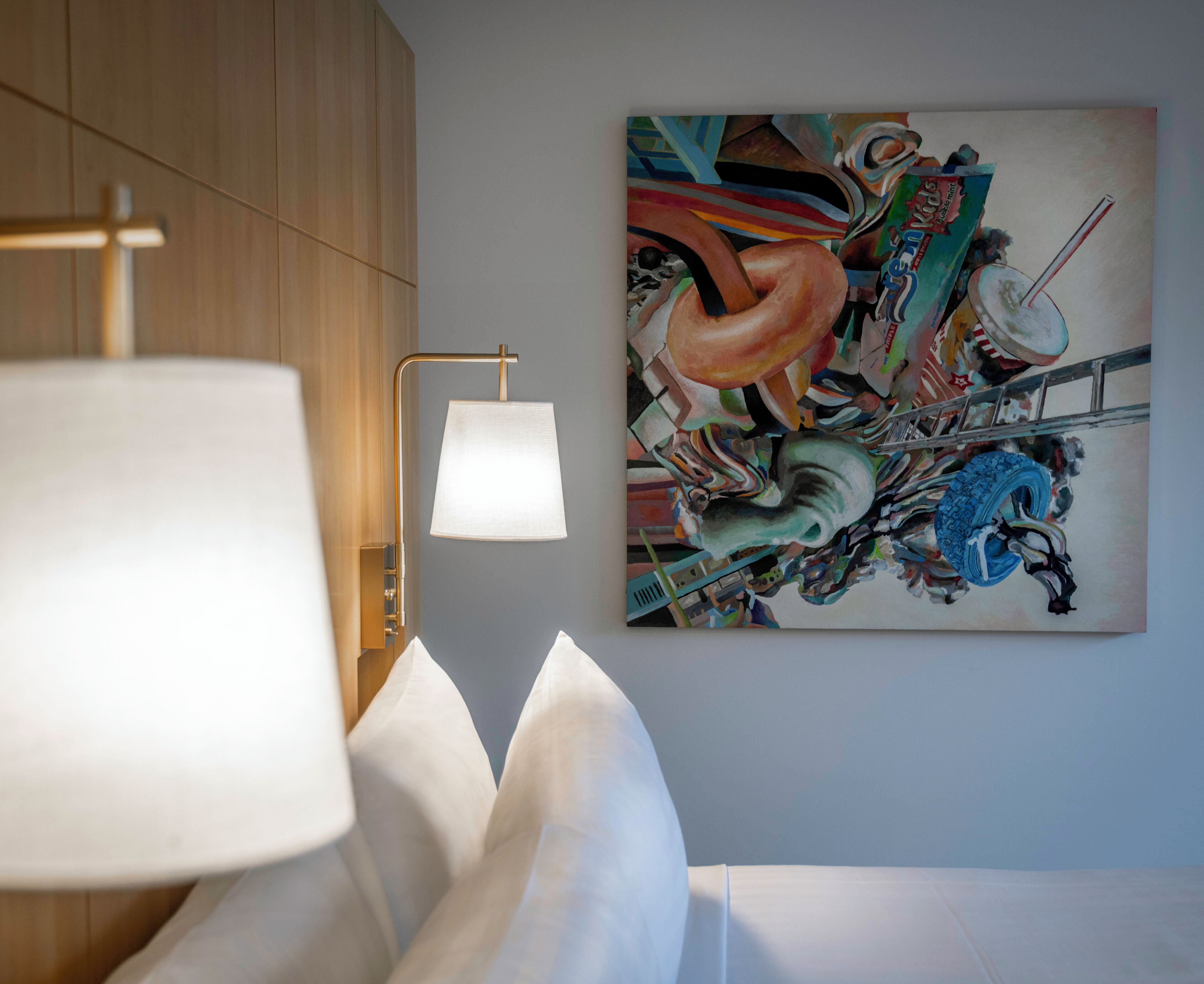 Una habitación moderna con un cuadro abstracto grande en la pared, una lámpara de noche y una cama bien hecha.