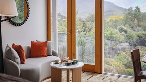 A living room with a sofa, a coffee table, and a view of a mountainous landscape through a sliding glass door. - Islington Hotel (South Hobart)