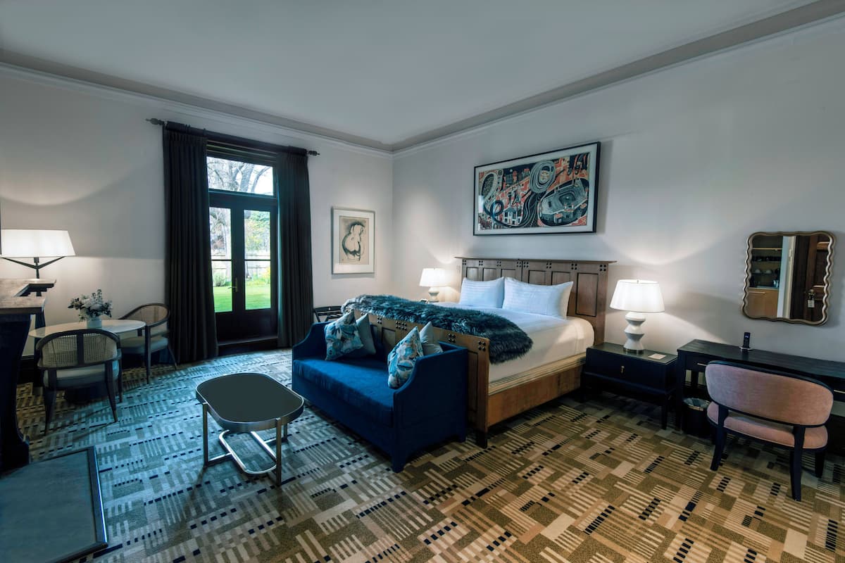 A hotel room with a bed, a desk, a chair, a sofa, and a window with curtains.